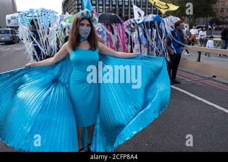 Extinction Rebellion Aktivist mit blauen Flügeln und einer Gesichtsmaske, die aufsteigende Ozeane beim Marine Rebellion march am 6. September 2020 in London, Großbritannien, liest. Meeresaufstand, Meereslebewesen, Tieraufstand und Aussterben die Meereslebewesen haben sich zusammengetan, um die Artenvielfalt in unseren Meeren zu feiern und um die Zerstörung der Ozeane und der Meereslebewesen durch den Klimawandel und menschliche Einmischung zu trauern, Und den Verlust von Menschenleben, Häusern und Lebensgrundlagen durch den steigenden Meeresspiegel. Extinction Rebellion ist eine 2018 gestartete Gruppe zum Klimawandel und hat eine große Gruppe von p gewonnen Stockfoto