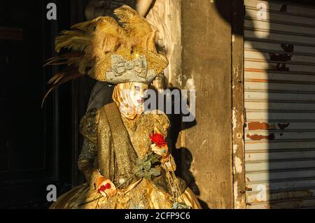 VENEDIG, ITALIEN - 16. FEBRUAR 2015: Romantische Maske mit roter Rose zwischen Sonnenstrahlen und Schatten auf dem Markusplatz während des Karnevals. Der Karneval in Ve Stockfoto