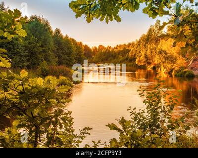 Kleiner Waldfluss bei Sonnenuntergang im Herbst. Schöne Landschaft, Sonnenuntergang auf dem Fluss. Goldener Sonnenuntergang am Fluss. Natur Hintergrund Stockfoto