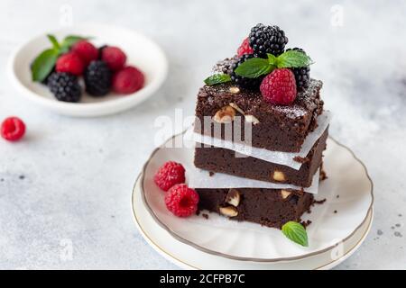 Nahaufnahme von köstlichen Schokolade Brownie quadratische Stücke mit Haselnüssen, dekoriert mit Himbeeren und Brombeeren. Traditionelle hausgemachte Dessert. Stockfoto