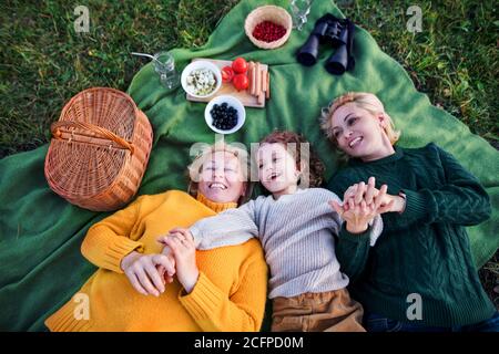 Draufsicht auf kleine Mädchen mit Mutter und Großmutter mit Picknick in der Natur. Stockfoto