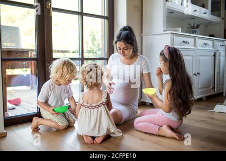Schwangere Frau mit kleinen Kindern drinnen zu Hause, reden. Stockfoto