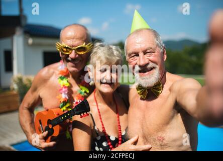 Gruppe von fröhlichen Senioren am Pool im Freien im Hinterhof, Selfie zu nehmen. Stockfoto