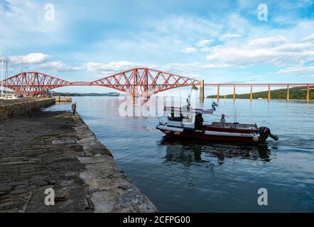 Der Ferry Flyer fährt in den Hafen von South Queensferry mit der Forth Rail Bridge dahinter. Stockfoto