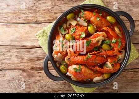 Ein Topf Huhn Marengo mit Krebsen, Pilzen, Oliven, Knoblauch, Tomaten und Schalotten Nahaufnahme in einem Topf auf dem Tisch. Horizontale Ansicht von oben Stockfoto