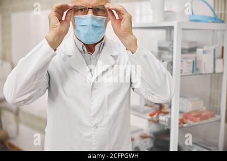 Ernsthafter Gesundheitsarbeiter in einem Laborkittel, der eine Brille aufsetzt Stockfoto