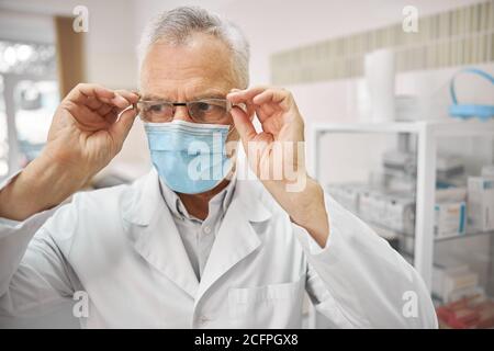 Professioneller Arzt in einer OP-Maske berührt seine Brille Stockfoto