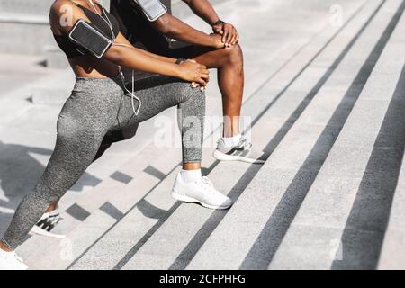 Unkenntlich schwarzes Paar in der Sportbekleidung zusammen trainieren im Freien, Dehnung Beinmuskeln Stockfoto