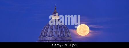 Petersdom Kuppel mit Vollmond im Hintergrund. Reale Ansicht des Mondes, der tatsächlich hinter dem Vatikan in Rom vorbeigeht Stockfoto