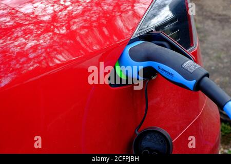 Rotes Elektroauto wird über Stromkabel aufgeladen Stockfoto