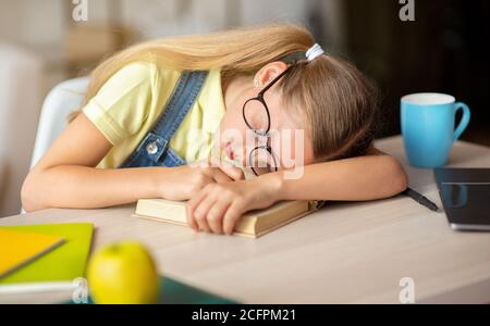 Müde Schulmädchen schlafen am Tisch mit Buch Stockfoto