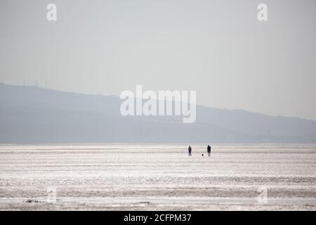 Zwei Menschen gehen mit ihrem Hund am West Kirby Beach Stockfoto