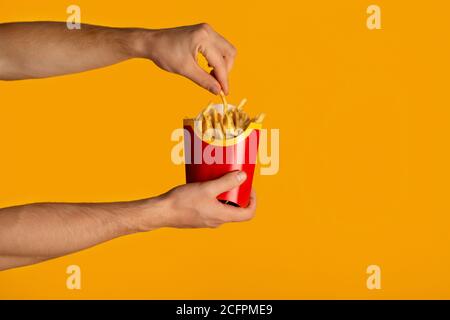 KHARKIV, UKRAINE - 4. APRIL 2020: Junger Mann hält Packung pommes von McDonald's auf orangefarbenem Hintergrund, Nahaufnahme Stockfoto