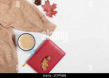 Tasse Kaffee, warmer Herbstpullover und Buch auf weißem Holzhintergrund. Herbstkomposition. Stockfoto