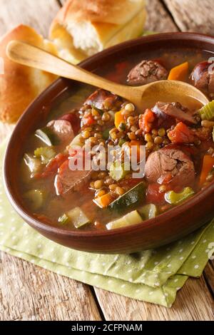 Linsensuppe mit Würstchen, Tomaten, Zucchini, Sellerie und Karotten in Nahaufnahme auf einem Teller auf dem Tisch. Vertikal Stockfoto
