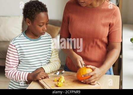 Nicht erkennbare Frau, die an der Küchentheke steht und ihrem Sohn vorführt, wie es geht Kürbis für Halloween schnitzen Stockfoto