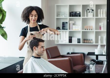 Millennial Kerl sitzt bei Friseuren und immer Frisur aus afrika amerikanischer Meister Stockfoto