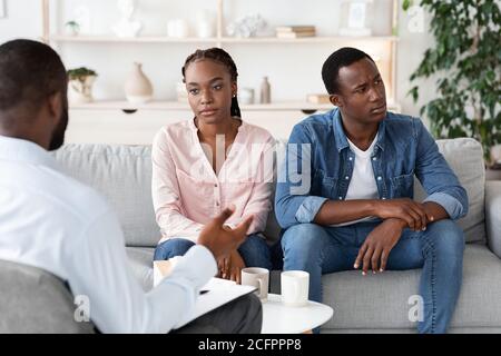 Paartherapie. Depressive afrikanische Ehegatten sitzen auf der Couch im Büro des Beratershelters Stockfoto