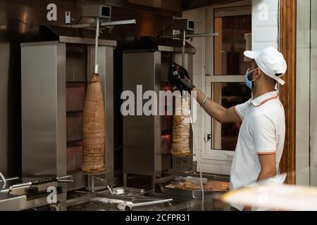 Uniformierter Koch, Schneiden und Zubereiten Huhn und Rindfleisch Döner Kebabs mit einer Prävention Gesichtsmaske an einem Fast-Food-Stand Stockfoto