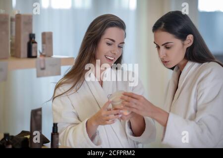 Zwei hübsche Frauen diskutieren neue Creme und schauen aufgeregt Stockfoto