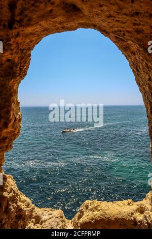 Ein Bild von einem Felsenfenster in Algar Seco Algarve, Portugal mit Blick auf ein türkisfarbenes Meer mit einem Boot Stockfoto