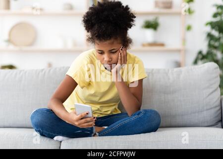 Gelangweilt African American Teen Mädchen Mit Smartphone Sitzen Zu Hause Stockfoto