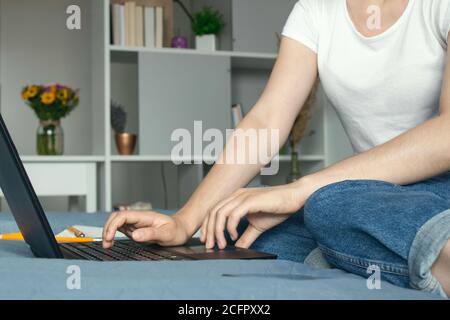 Nahaufnahme von jungen Geschäftsfrau, Lehrerin oder Studentin, die online auf ihrem Bett mit Handy und schwarzem Laptop arbeitet oder studiert. Fernarbeiten von zu Hause Stockfoto