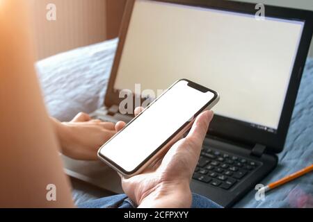 Mockup Bild der Frau Hand hält Handy mit weißem leeren Bildschirm, sitzt vor dem schwarzen Laptop mit leerem Bildschirm - Online-Shopping, netwo Stockfoto