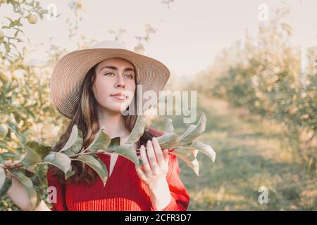 Porträt im Garten. Junge und schöne Frau in einem Hut und einem roten Kleid, mit einem Baum Zweig in den Händen.Copy Space. Stockfoto