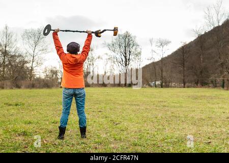 Suchen Sie mit EINEM Metalldetektor. Die junge Frau fand einige Schätze in der Nähe des Flusses. Der Blick von hinten. Stockfoto