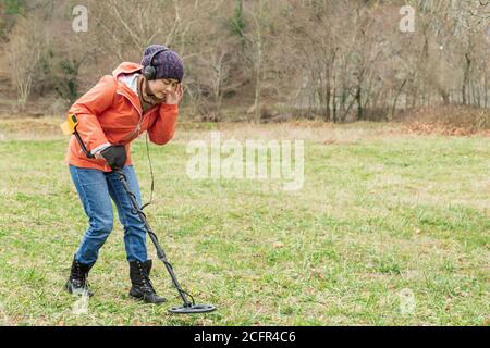 Die junge Frau erkundet mit einem Detektor begeistert den Boden. Stockfoto