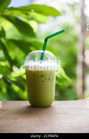 eisgetränke grüner Tee Smoothie / Matcha grüner Tee mit Milch auf Plastikglas auf dem Holztisch und Natur Grüner Hintergrund Stockfoto