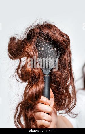 Die Hand einer Frau hält einen Kamm mit Augen und eine Perücke, die das Gesicht einer Person imitiert. Haarpflegekonzept. Stockfoto