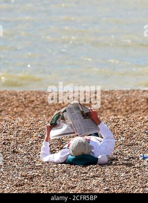 Brighton UK 7. September 2020 - Zeit, um eine Zeitung am Strand zu lesen, während Besucher die warme Herbstsonne an der Strandpromenade von Brighton heute genießen, da das wärmere Wetter für später in dieser Woche in ganz Großbritannien prognostiziert wird : Credit Simon Dack / Alamy Live News Stockfoto