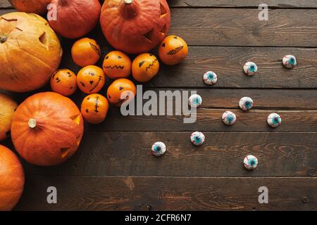 Top-down flach Lay Zusammensetzung aus geschnitzten Kürbisse, Mandarinen mit Jack o' Laternen Gesichter und gruselige Augapfel Süßigkeiten liegen auf Holztisch Stockfoto