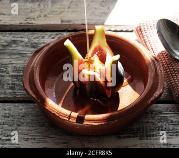 feige mit Feta-Käse in einer Keramikschale auf einem weißen Shabby Chic Holztisch, Honig wird auf der Feige beträufelt Stockfoto