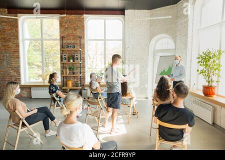 Männlicher Sprecher, der in der Halle des Universitätsworkshops vorstellte. Publikum oder Konferenzsaal. Junge Studenten, Teilnehmer im Publikum tragen Gesichtsmaske. Wissenschaftliche Konferenz Veranstaltung, Ausbildung. Bildung Stockfoto