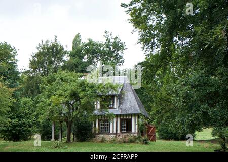 Kleines freistehendes Normannisches Fachwerkhaus mit Schiefer-Ziegeldach umgeben Bei Bäumen im Garten Stockfoto