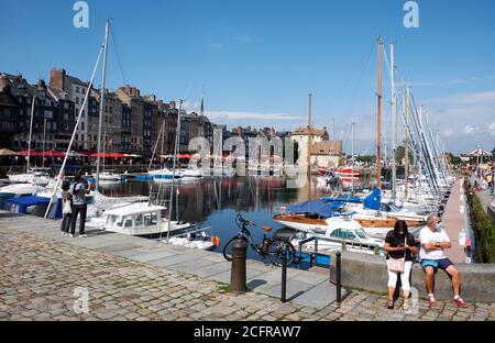 Pärchen, die während des COVID-19 an der Wand sitzen und Gesichtsmasken tragen Pandemie in der malerischen Hafenstadt Honfleur in der Normandie Stockfoto