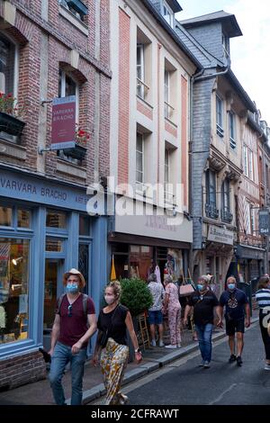 Urlauber und Touristen in der Einkaufsstraße tragen Gesichtsmasken während Die COVID-19 Pandemie in der malerischen Hafenstadt Honfleur In der Normandie Stockfoto