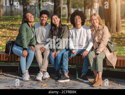 Gruppe positiver Freunde, die auf der Bank sitzen und lächeln Stockfoto