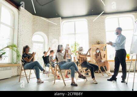 Männlicher Sprecher, der in der Halle des Universitätsworkshops vorstellte. Publikum oder Konferenzsaal. Junge Studenten, Teilnehmer im Publikum tragen Gesichtsmaske. Wissenschaftliche Konferenz Veranstaltung, Ausbildung. Bildung Stockfoto