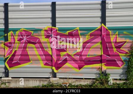 Violette, gelbe und rosa Graffiti an einer Lärmschutzwand Stockfoto