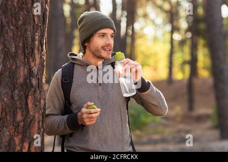 Hübscher Kerl, der Wasser trinkt, während er durch den Wald geht Stockfoto