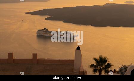 Ein Kreuzfahrtschiff vor Anker in der Bucht von Fira auf der Insel Santorini in Griechenland bei Sonnenuntergang. Stockfoto