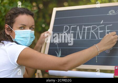 Zurück zur Schule. Back to School (in Französisch) geschrieben auf Klassenzimmer Kreidetafel von Lehrer mit Gesichtsmaske. Klassenraum im Freien aufgrund von covid-19. Stockfoto