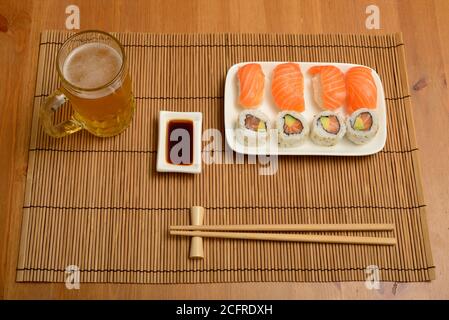 Essstäbchen, Sojasauce, Sushi und ein Glas Bier auf der Bambusmatte Stockfoto