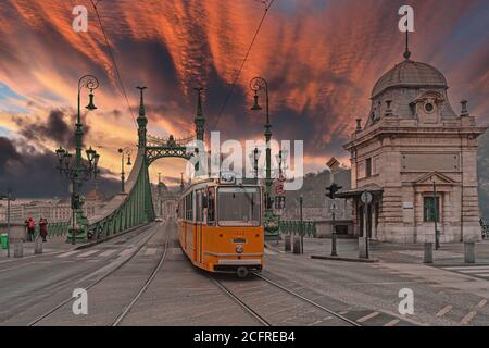 Historische Straßenbahn auf der Freiheitsbrücke in Budapest, Ungarn. Stadt bei Sonnenuntergang Stockfoto