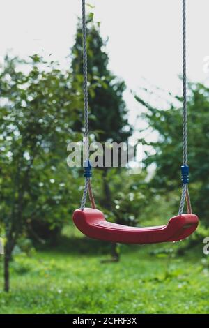 Einsame rote und nasse hängende Schaukeln im grünen Garten Hintergrund Während des bewölkten Tages im Herbst Stockfoto