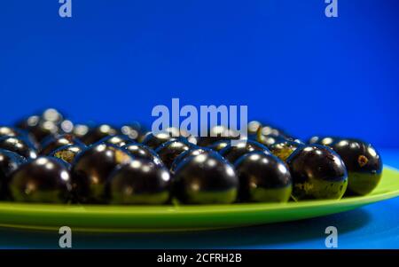 Jaboticaba Früchte (Myrciaria cauliflora) auf einem grünen Teller serviert. Blauer Hintergrund. Jabuticaba Bäume sind Bäume, die in fast allen Brazi gefunden werden können Stockfoto